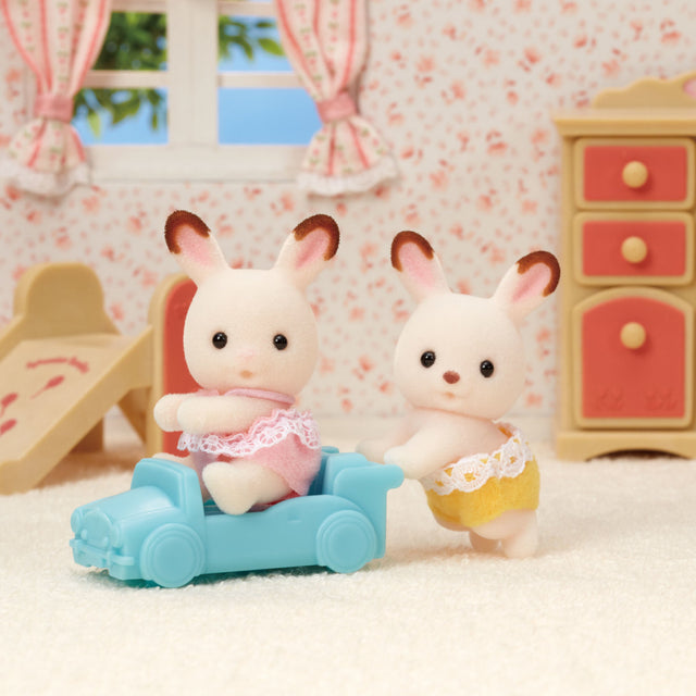 Chocolate Rabbit Twins plush toys in a cozy playroom setting with pastel furniture and floral wallpaper.