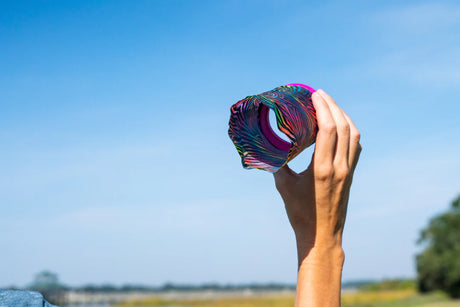 Hand holding colorful Waboba Airlyft glider in blue sky, lightweight fabric flying toy designed for outdoor play.