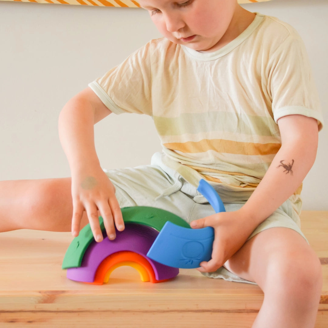 Child playing with colorful silicone arches stacking toy Over the Rainbow | Bright on wooden surface.