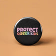 Button | Protect Queer Kids with colorful text on black background, expressing support and protection for queer children.