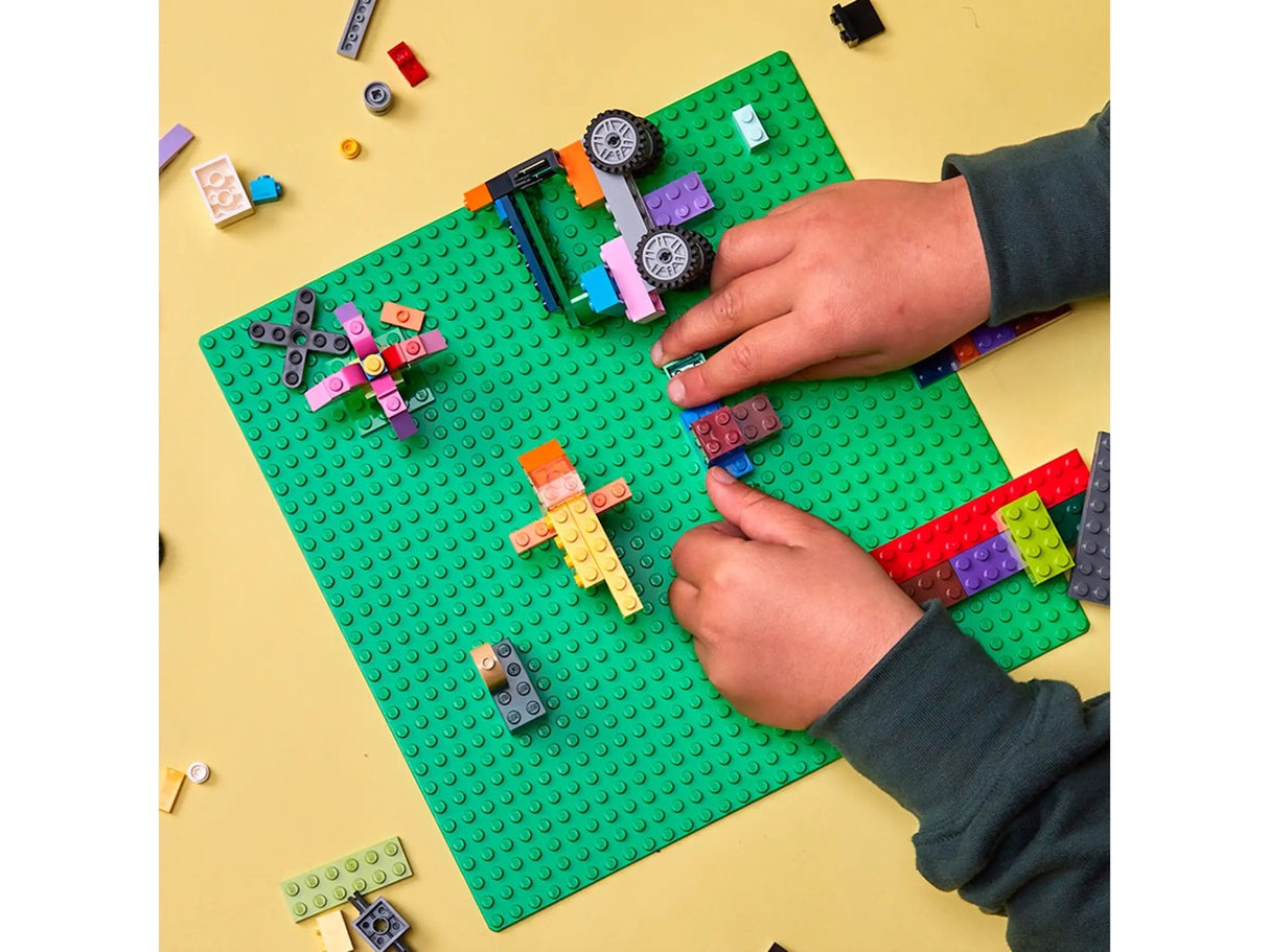 Classic Green Baseplate showing a child's hands building colorful LEGO creations on a 32x32 stud green building surface.