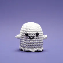 Small white crocheted ghost with black eyes and smiling mouth against a purple background