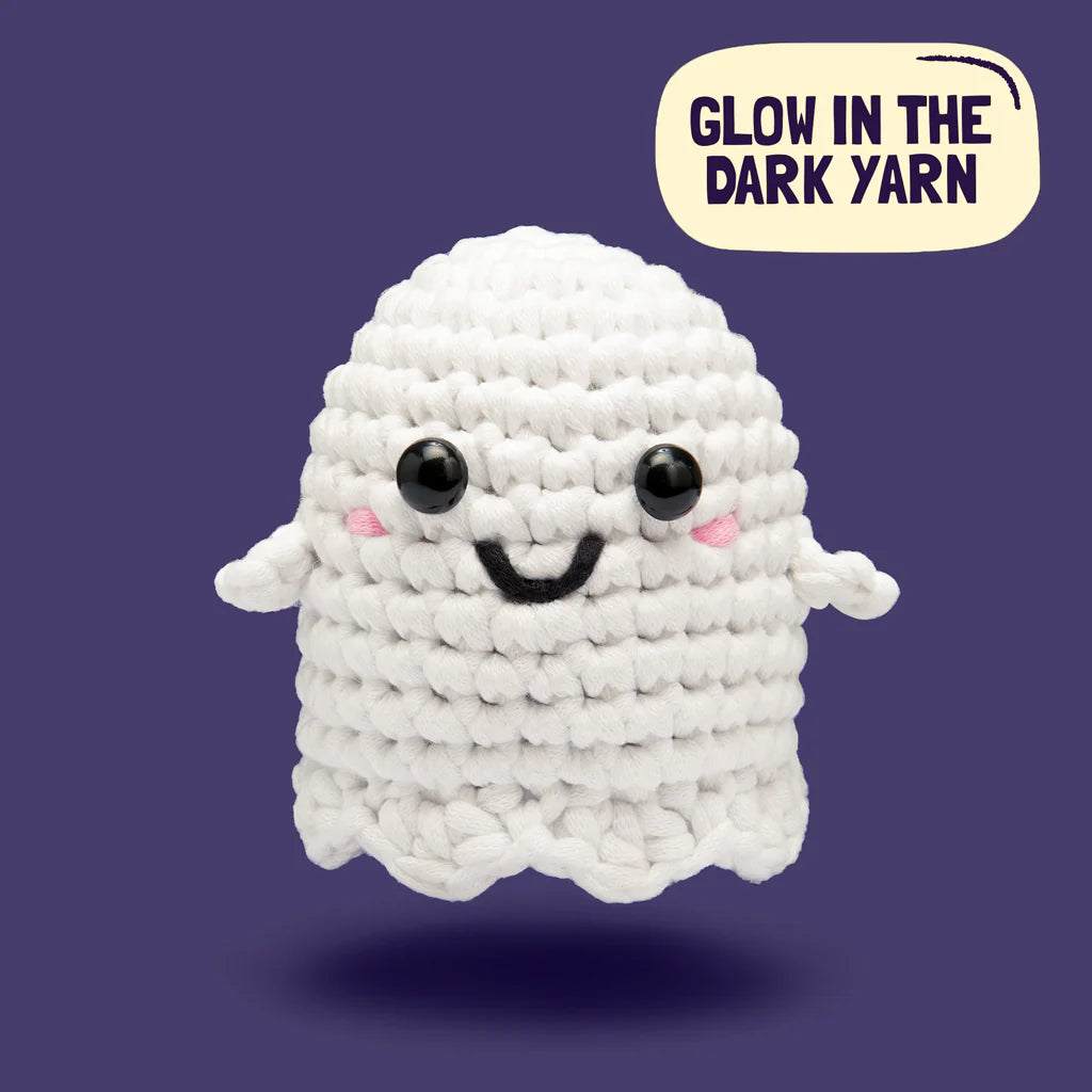 Cute crocheted ghost with black eyes and rosy cheeks made from glow-in-the-dark yarn on purple background