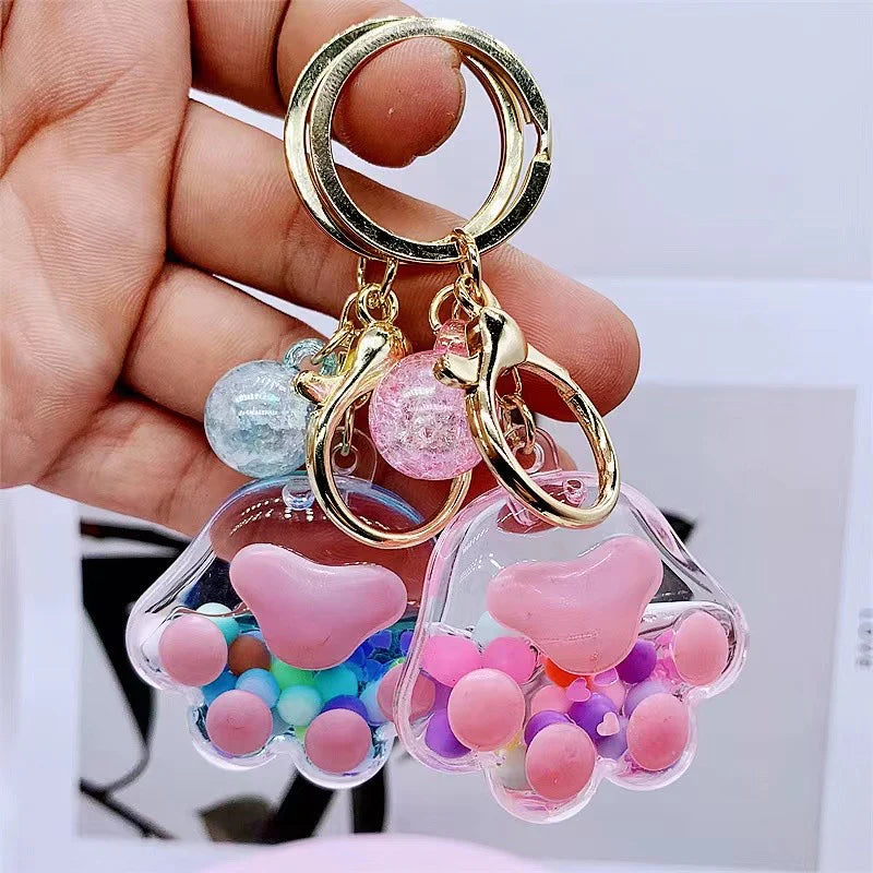 Hand holding two colorful Paw Floaty KeyChain accessories with keyrings and clips for easy attaching.