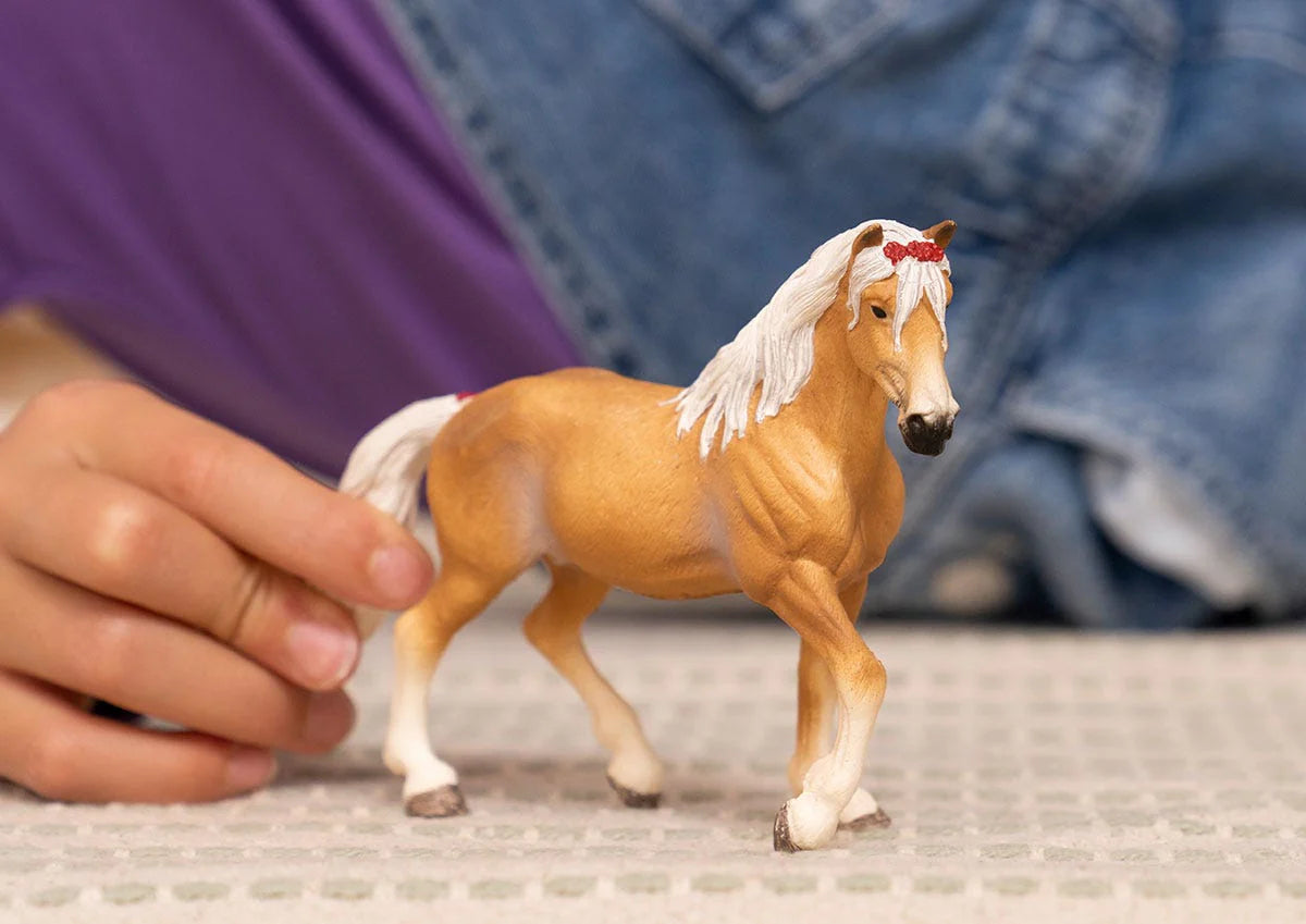 Horse Haflinger Mare figurine with a red bow in its white mane, trotting happily across the meadow.