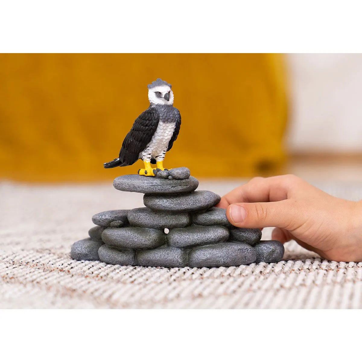 Harpy Eagle toy figure perched on stacked gray stones with a child's hand nearby for imaginative play.
