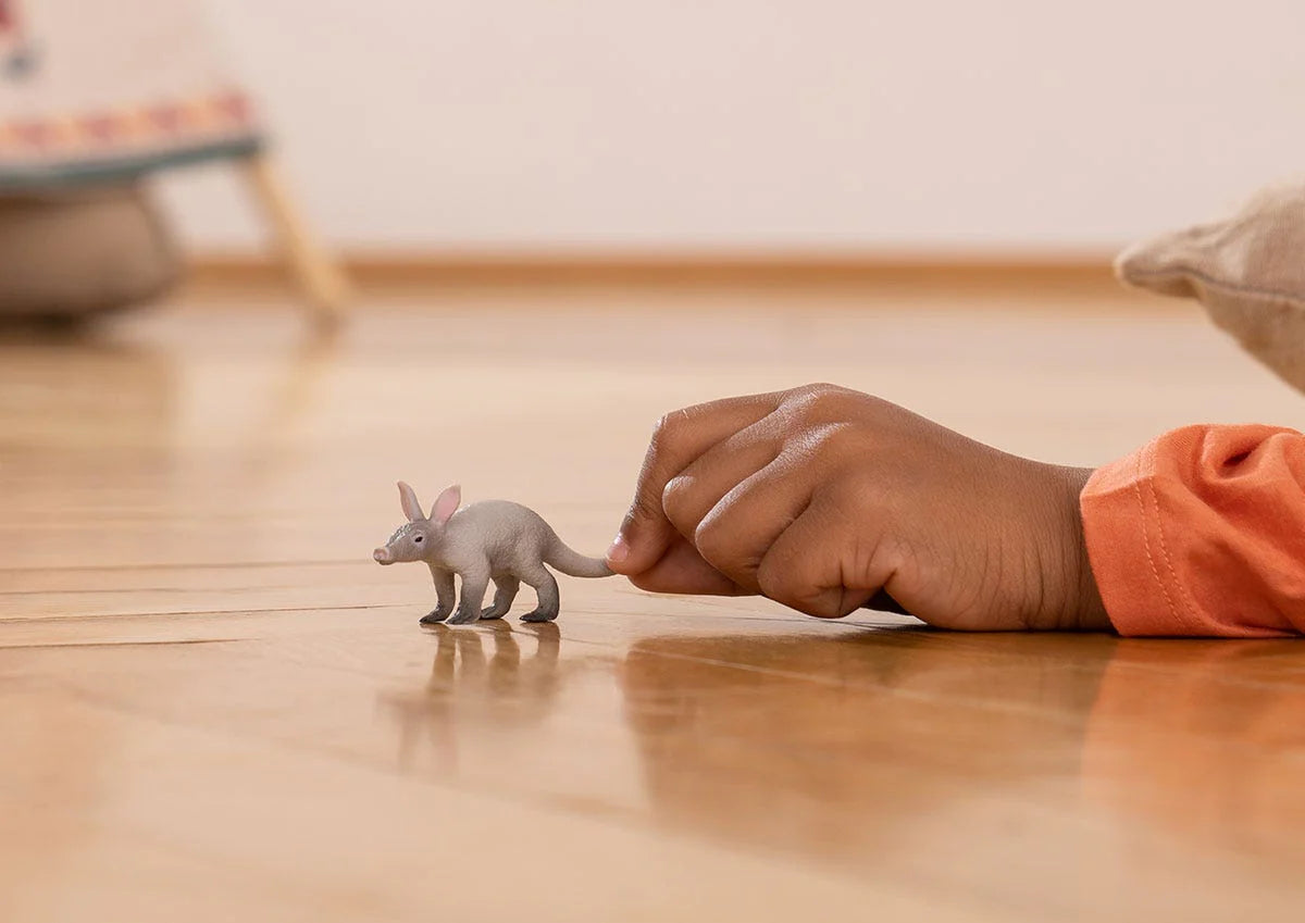 Child’s hand playing with a small Aardvark figurine on a wooden floor in a cozy indoor setting.