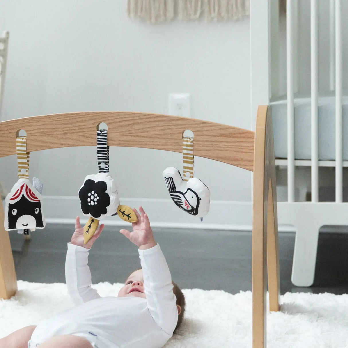 Organic Stroller Toy | Bird with embroidered center and crinkly leaves hanging on wooden frame above baby on rug.