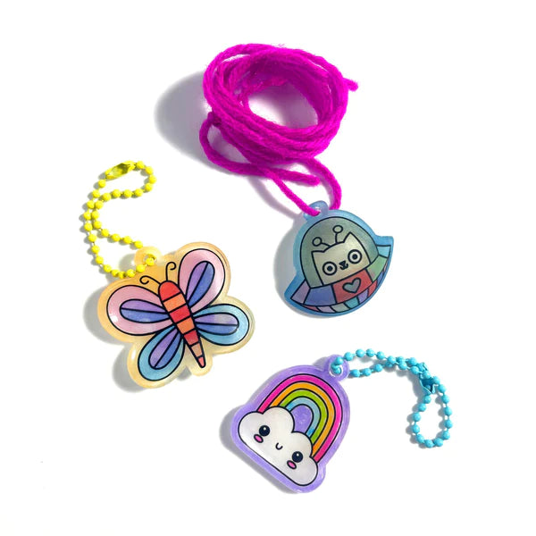 Shrink-Its! Cute Crew showing three colorful shrink plastic charms with ball chains and a pink cord on white background.