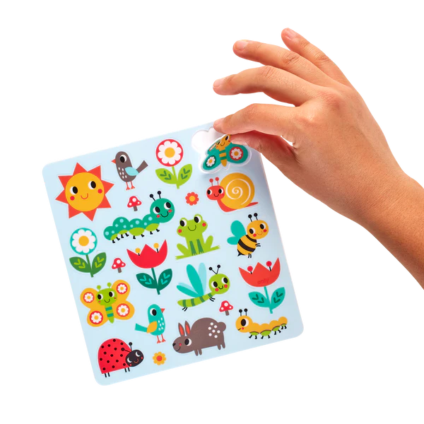 Hand placing a colorful butterfly sticker on reusable sheet from Play Again! Sunshine Garden activity book set.