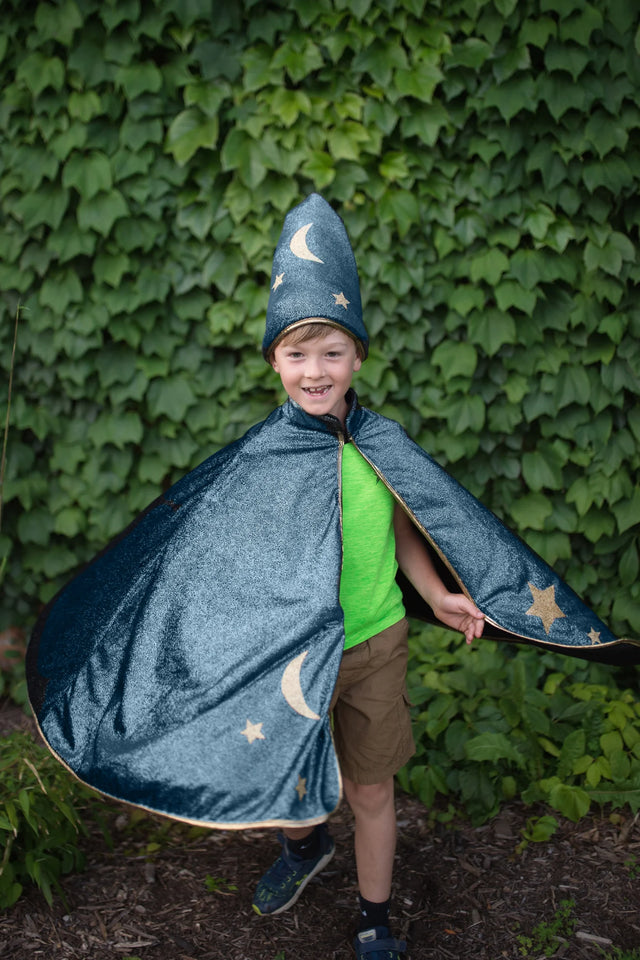 Child wearing Starry Night Wizard Cape & Hat with moon and star designs, playing outdoors with greenery background