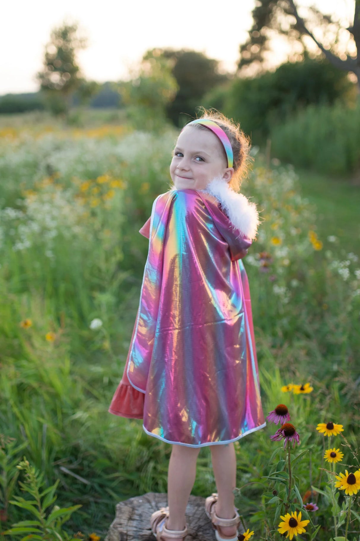Young girl outdoors wearing Rainbow Princess Cape with fluffy feather trim and shimmering rainbow colors.