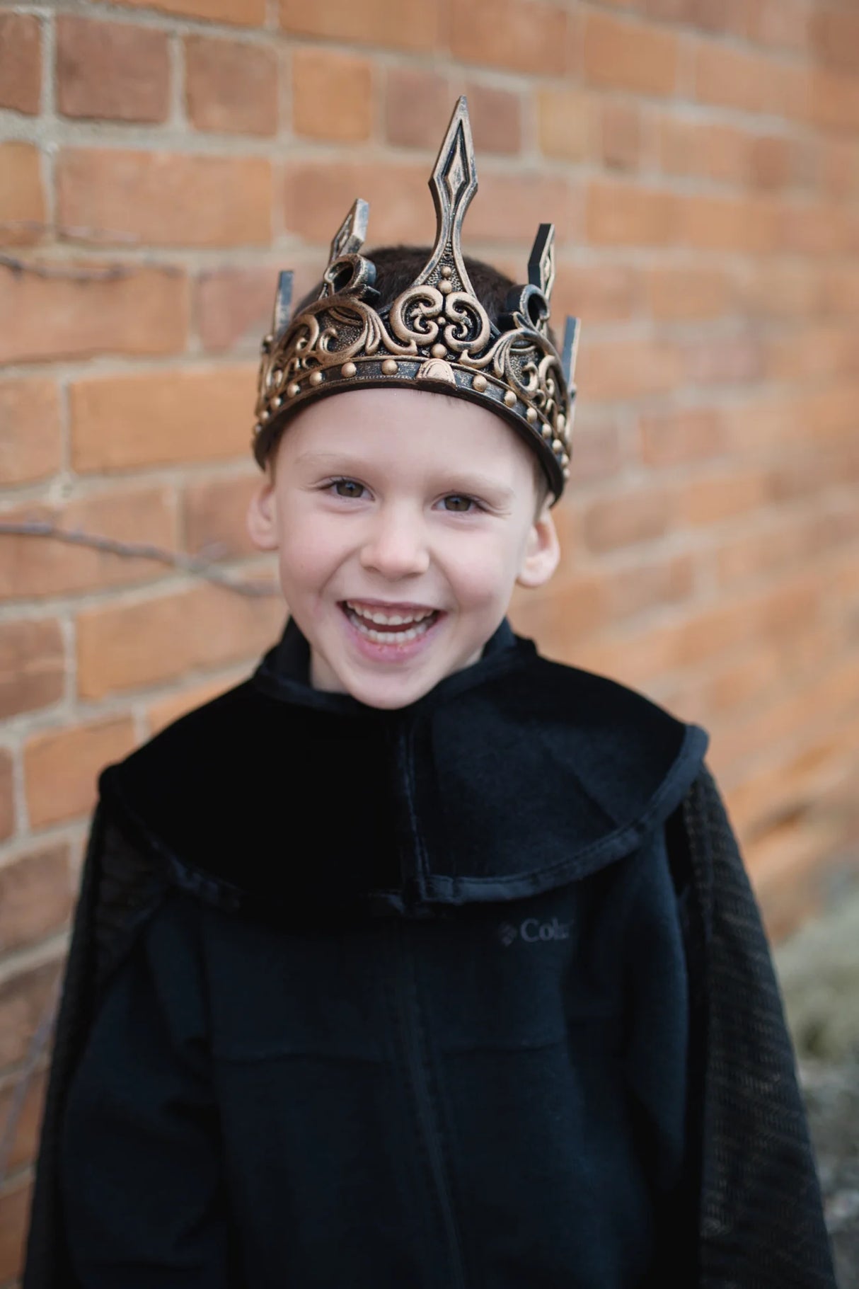 Medieval Crown | Gold/Black worn by smiling child, gold and black medieval style crown with ornate details against brick wall.
