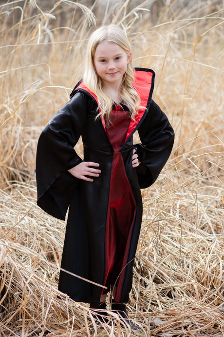 Young girl wearing Vampire Dress | Size 5-6 with black cloak and red interior standing outdoors in tall grass.