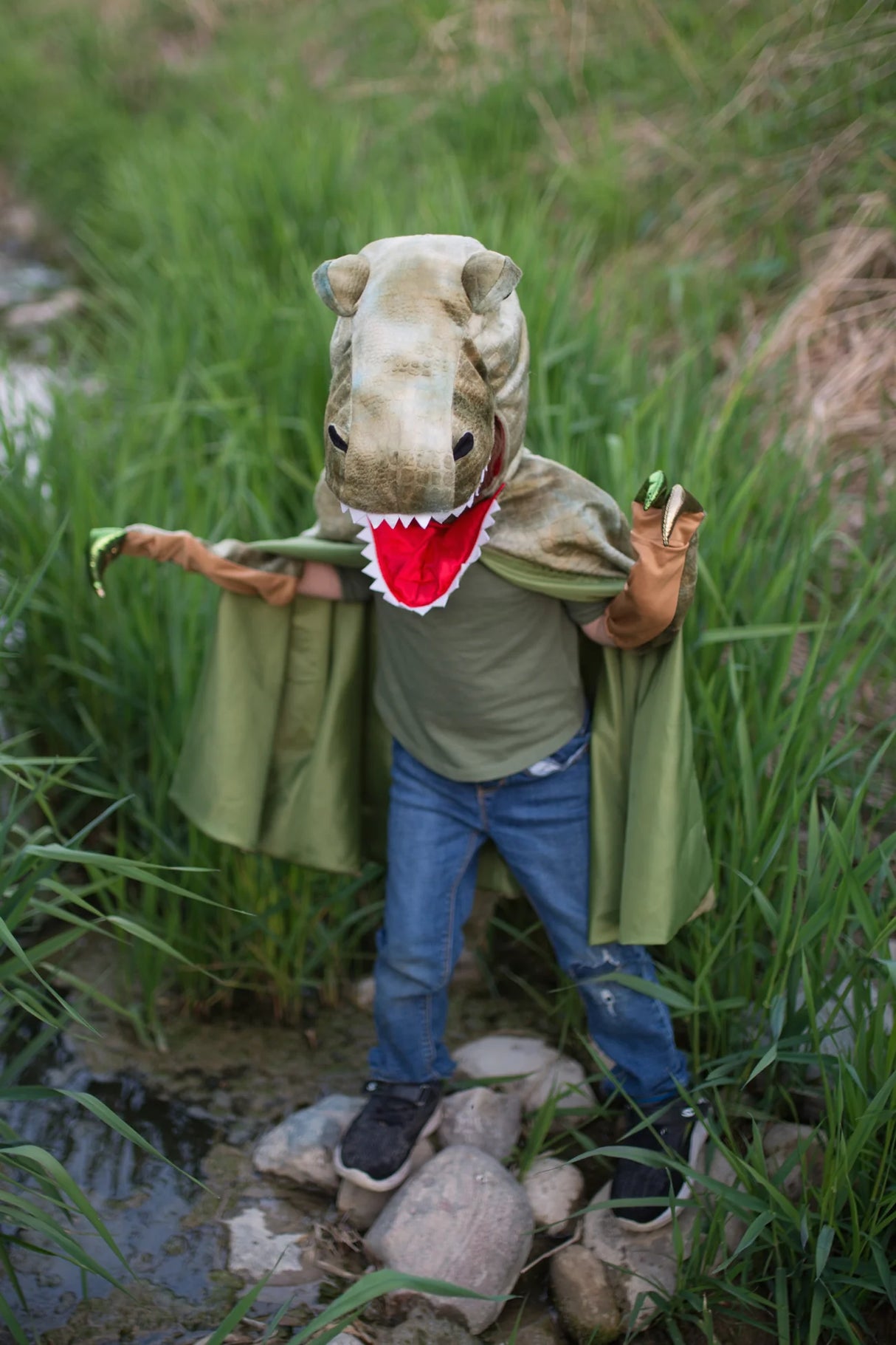 Child wears Grandasaurus T Rex Cape with Claws, featuring a full dinosaur head and matching claws outdoors.