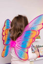 Child wearing Glitter Rainbow Wings with vibrant pink, blue, and orange hues and satin lined elastic for comfort.