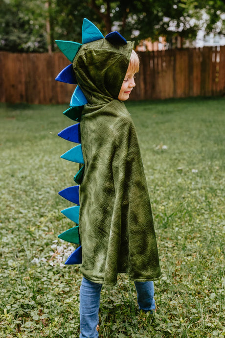 Child wearing the Dragon Cape with Claws in green crushed velvet with colorful textured spikes on the hood and back outdoors.