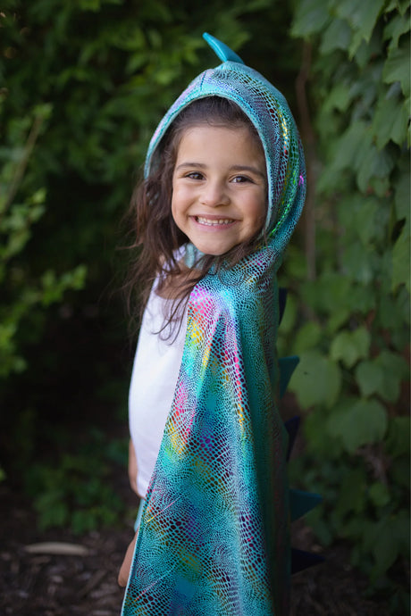 Smiling child wearing the Unicorn Dragon Reversible Cape in shiny blue dragon scales with hood and spikes outdoors.