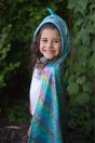 Smiling child wearing the Unicorn Dragon Reversible Cape in shiny blue dragon scales with hood and spikes outdoors.