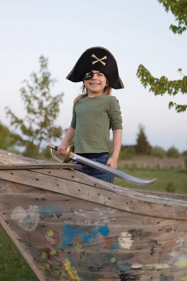 Child wearing a Pirate Captain Hat with gold trim and crossbones, smiling on a wooden play ship outdoors.
