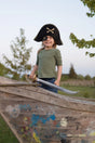 Child wearing a Pirate Captain Hat with gold trim and crossbones, smiling on a wooden play ship outdoors.