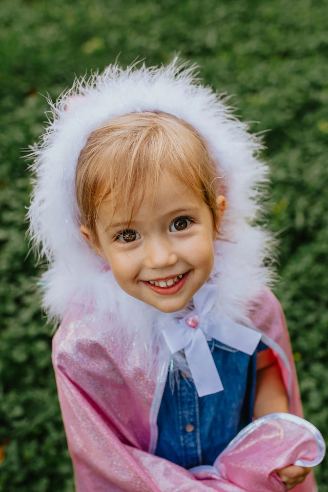 Smiling girl wears a pink Glitter Princess Cape with white marabou-trimmed hood and satin bow fastened with gem.