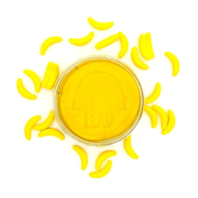 KidDough Glitter | Yellow in a container surrounded by small yellow banana-shaped dough pieces on a white background.