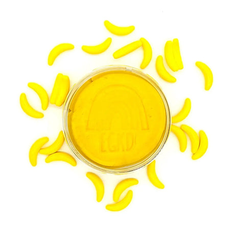 KidDough Glitter | Yellow in a container surrounded by small yellow banana-shaped dough pieces on a white background.