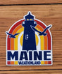 Maine Retro Lighthouse Magnet with vintage lighthouse, colorful sunset, and seagulls design on wood background.