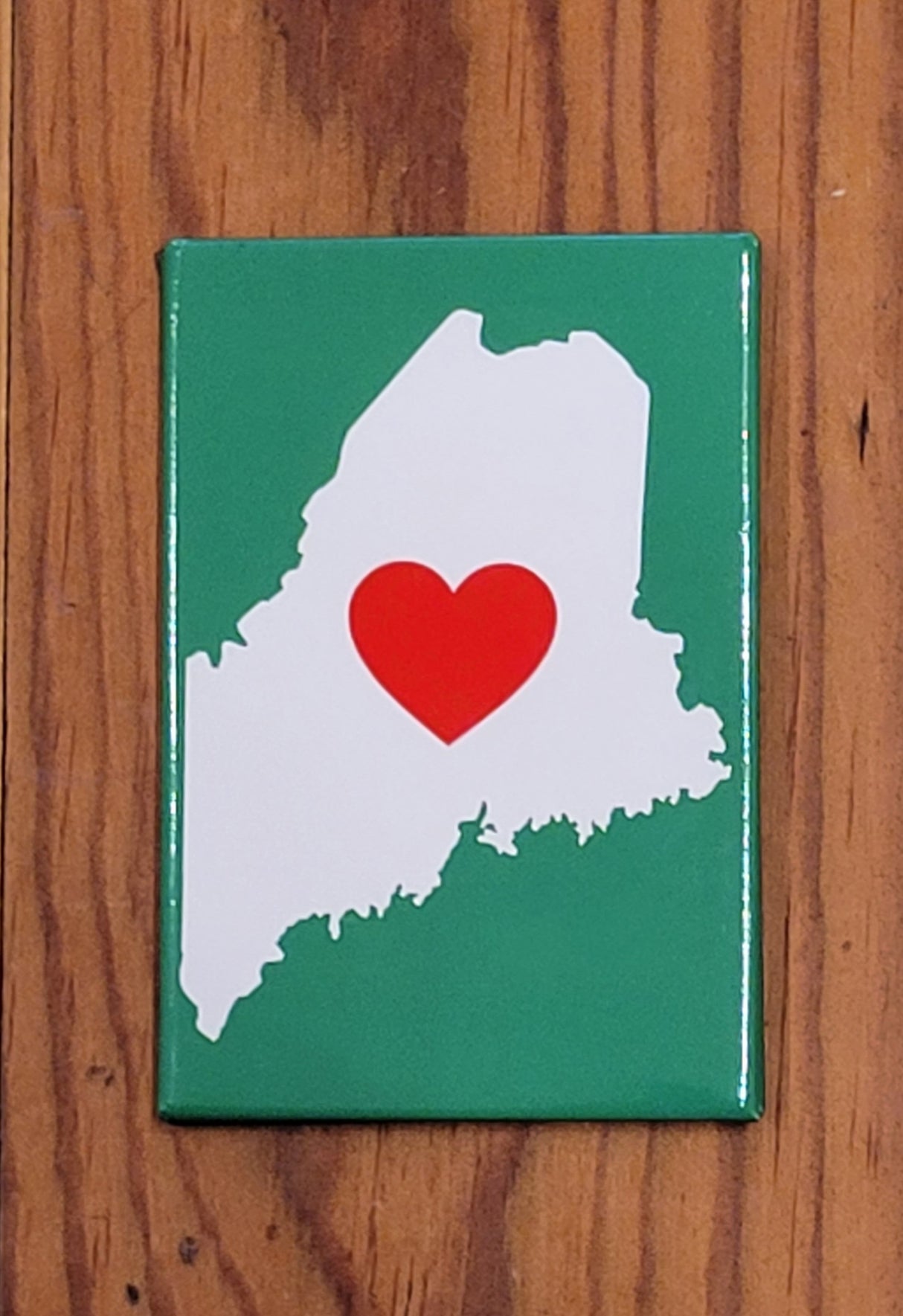 Maine Heart Magnet with white state outline and red heart on green background, perfect for fridge or magnetic surfaces.