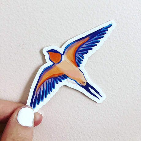 Hand holding a colorful Barn Swallow Sticker with orange and blue wings, designed by Gray Day Studio, 4 inches.