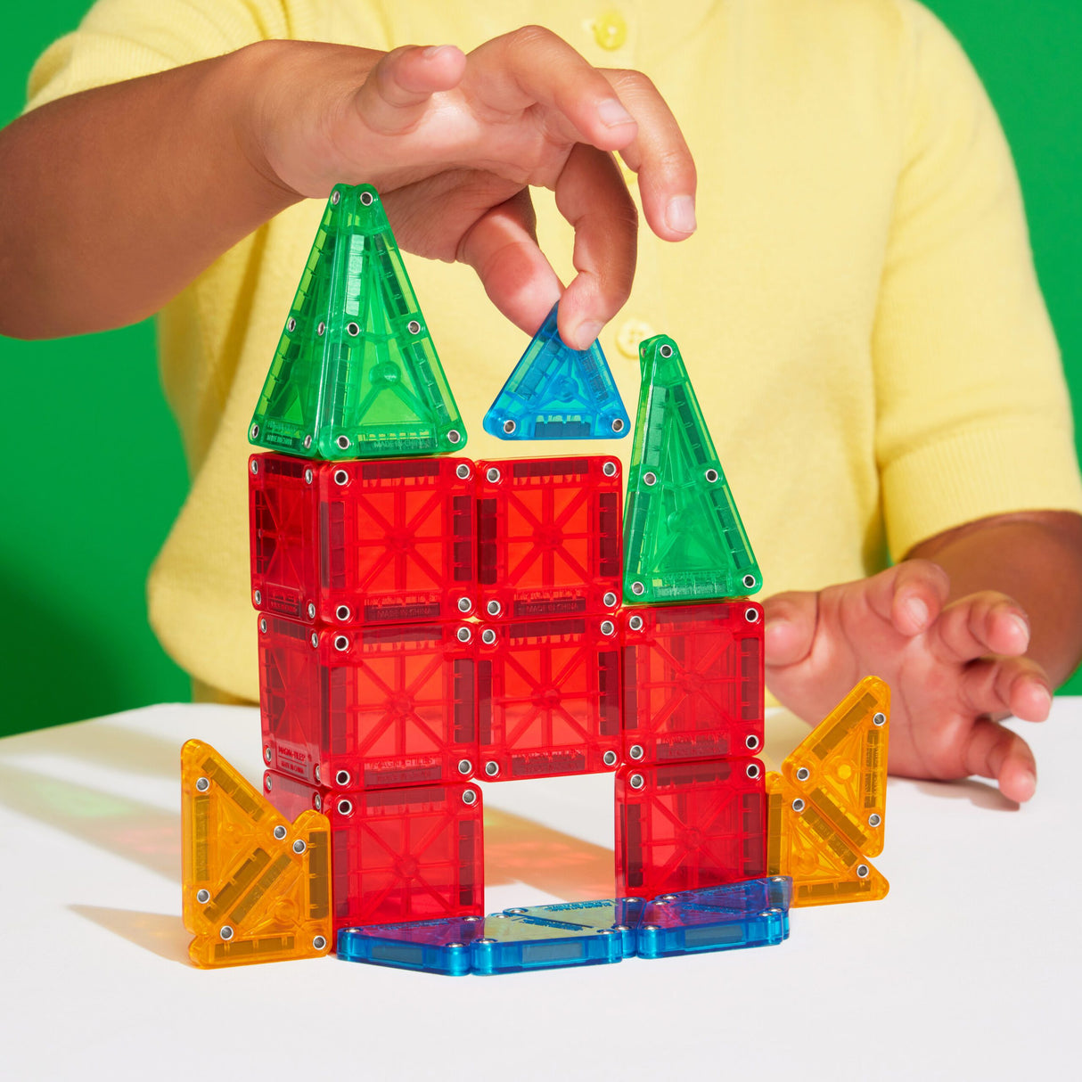 Child building colorful geometric shapes with Magnatiles Micromags Travel Set small magnetic tiles on table