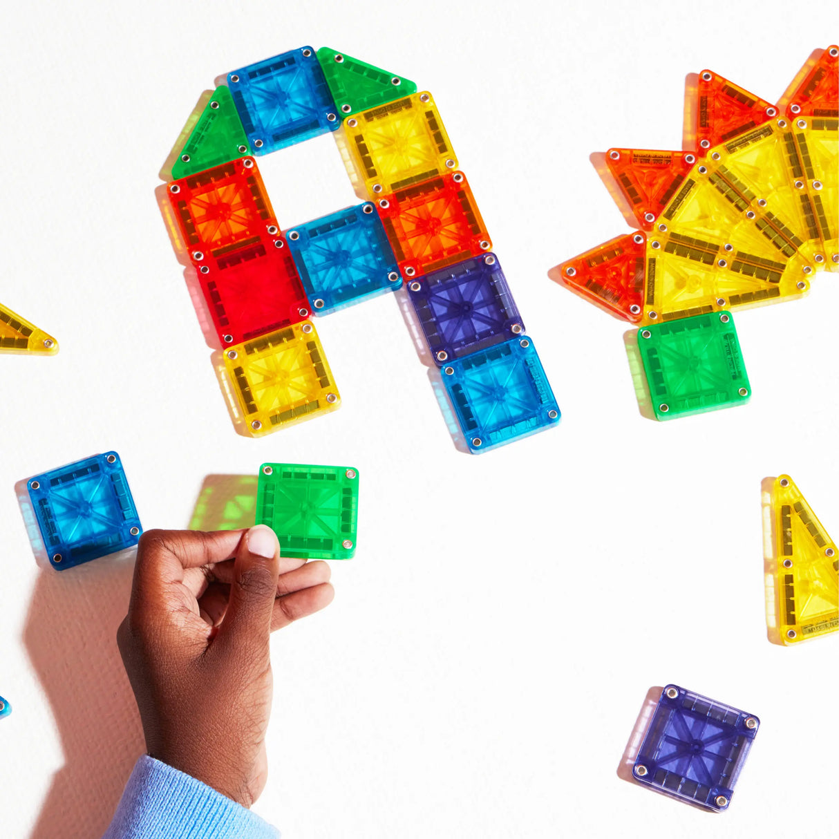 Hand holding colorful magnetic pieces arranging shapes with Magnatiles Micromags on white background.