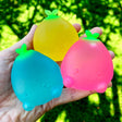 Hand holding three colorful Super Duper Sugar Squisher Mini Fruits in blue, yellow, and pink with green leaves.