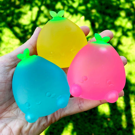 Hand holding three colorful Super Duper Sugar Squisher Mini Fruits in blue, yellow, and pink with green leaves.