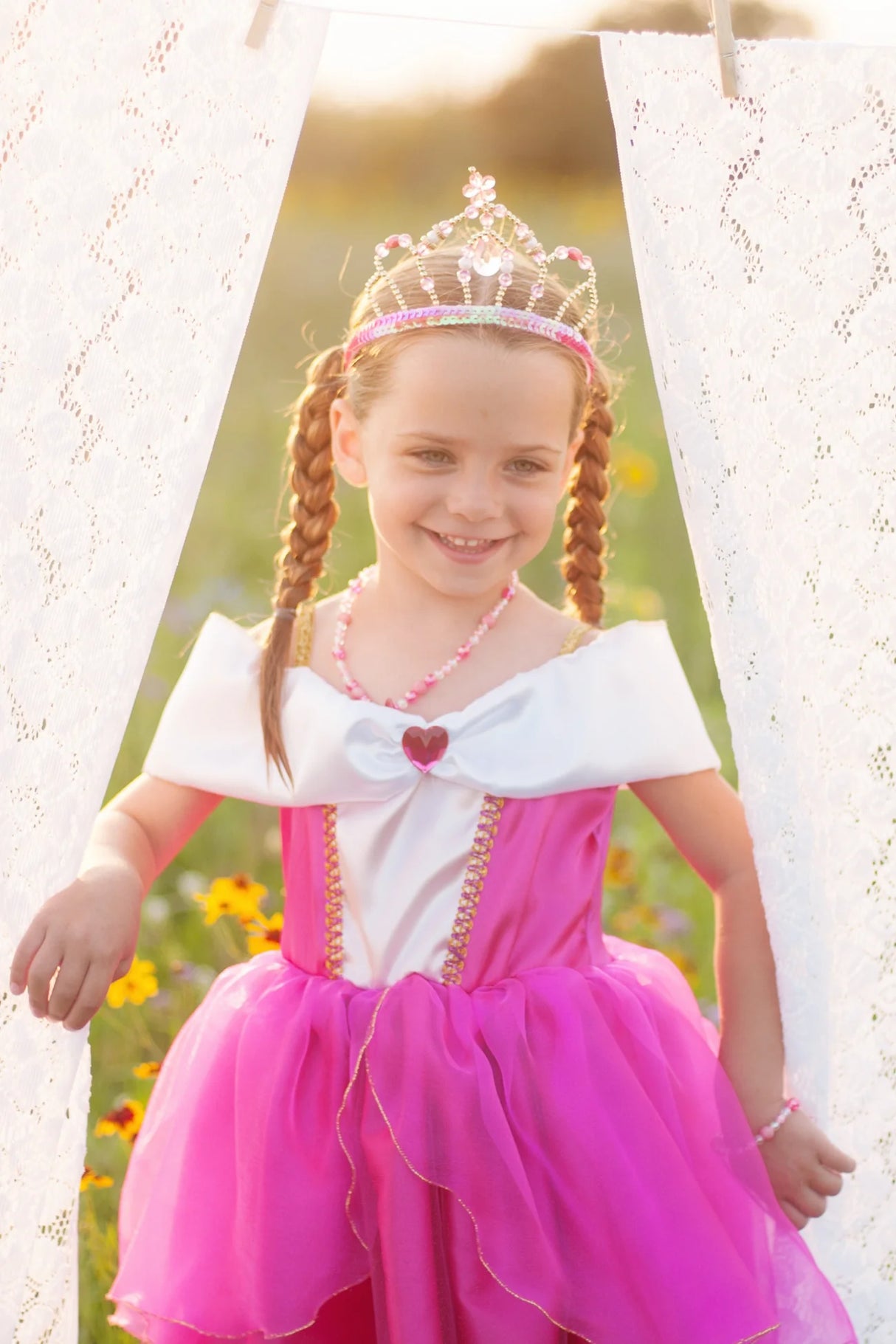 Young girl wearing a bright pink dress and the Fairy Princess Tiara with pink and magenta jewels outdoors.