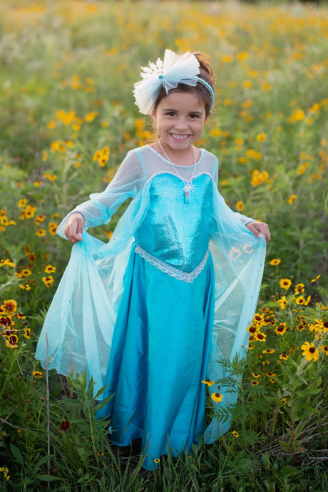 Young girl smiling outdoors wearing Ice Queen Dress with Cape | Size 5-6 in peacock blue satin and crystal organza sleeves.
