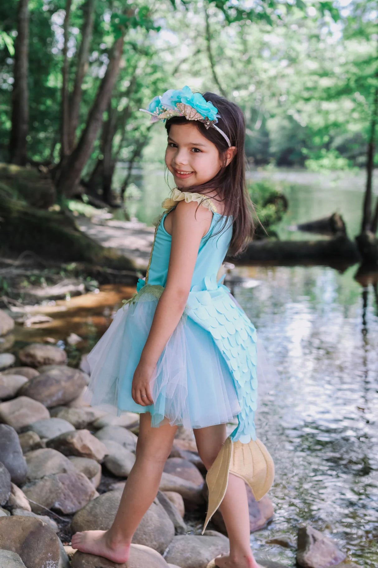 Girl wearing Mermalicious Dress with Tail in blue shimmer tulle with tailored scales and golden fin by a creek.