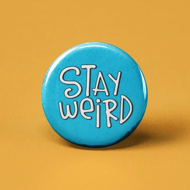 Button | Stay Weird round blue button with white playful text on a yellow background measuring 1.25 inches in diameter