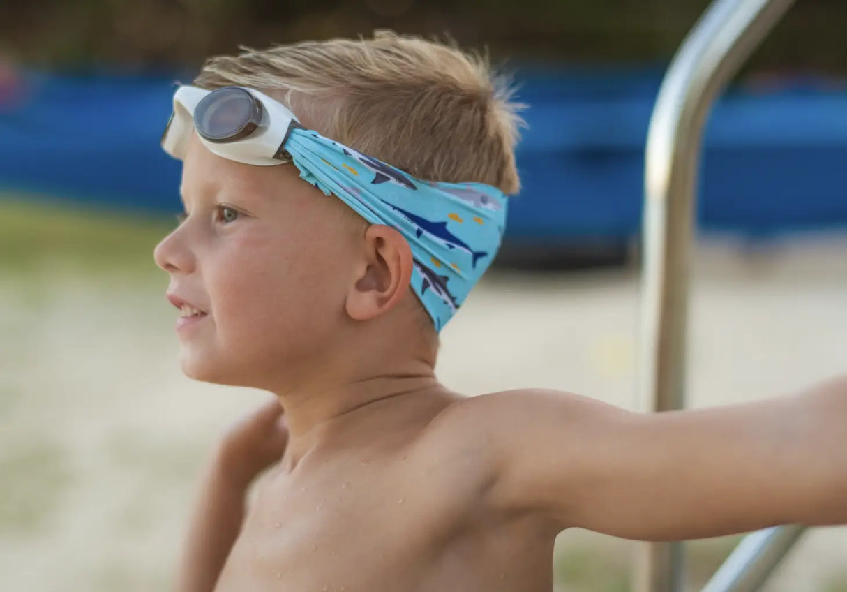 Child wearing Googles Shark Attack swim goggles with shark print strap and white frame by the pool.