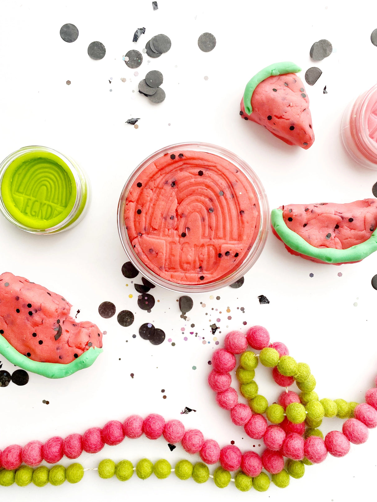 KidDough | Watermelon Slice with black glitter seeds in a container surrounded by watermelon-shaped dough pieces.