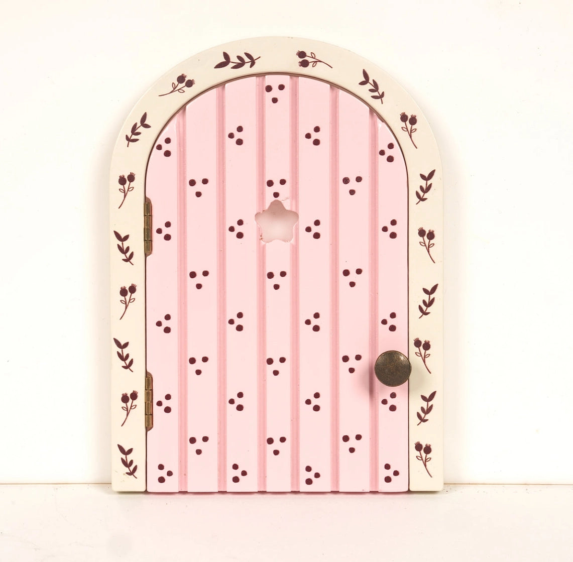 Small wooden fairy door painted pink with floral patterns and a tiny round knob for magical play spaces