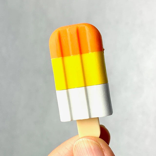 Hand holding a Japanese Eraser Ice Cream shaped like a colorful popsicle with orange, yellow, and white sections.