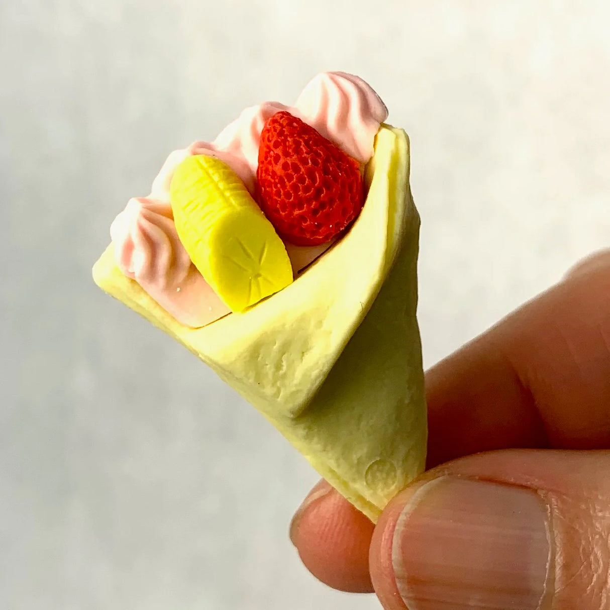 Close-up of a hand holding a tiny Japanese Eraser Cake eraser shaped like a crepe with fruit and cream toppings.