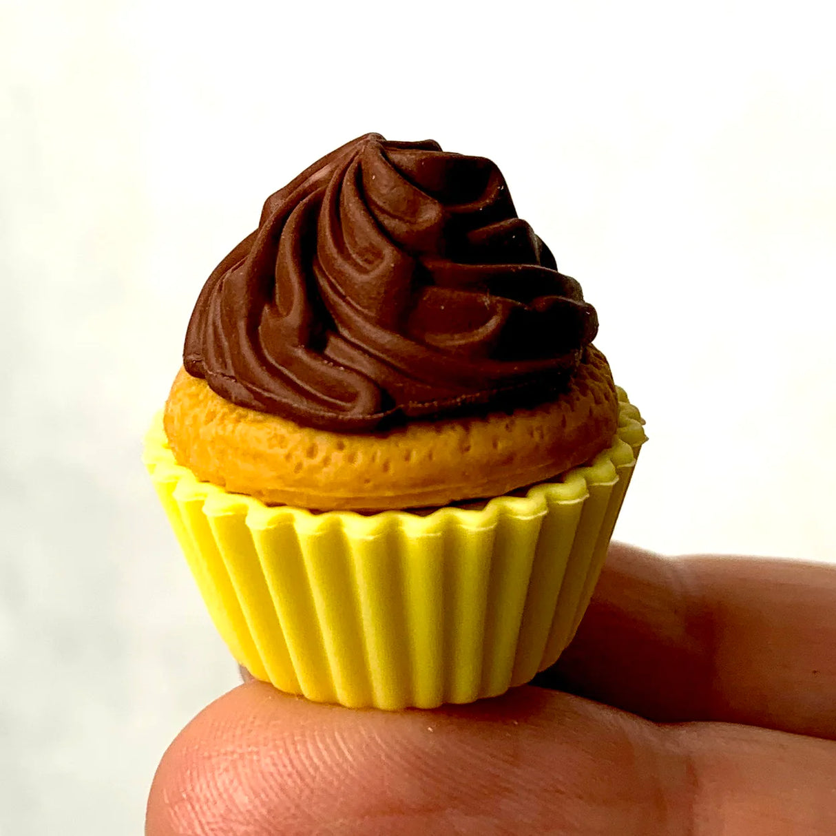 Close-up of a tiny cupcake eraser with chocolate frosting in a yellow cup, Japanese Eraser Cake held between fingers.