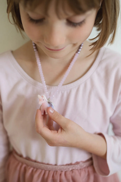 Child wearing a Fancy Unicorn Necklace with pink and purple beads and a small unicorn pendant with wings.
