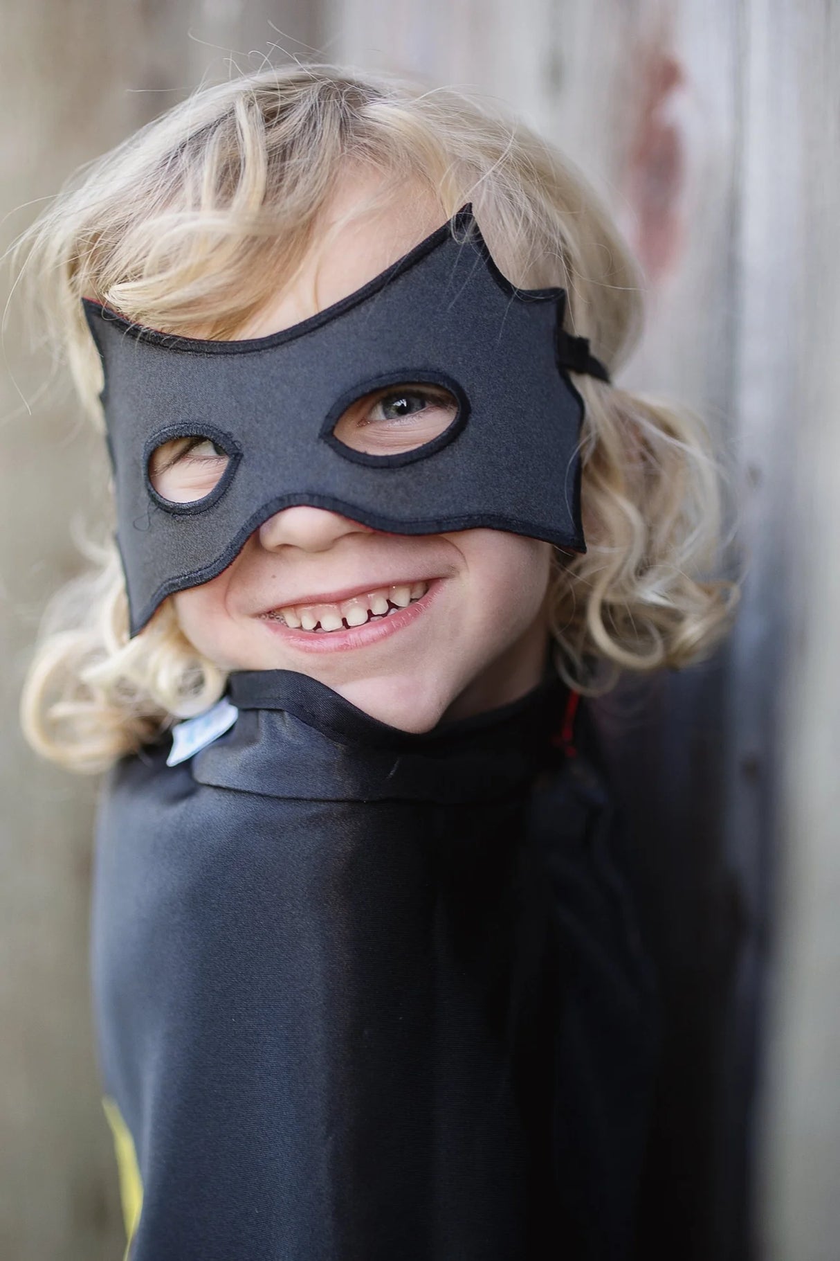 Child wearing the Spider Bat Reversible Cape & Mask Size 4-6 smiling with black satin cape and matching mask.