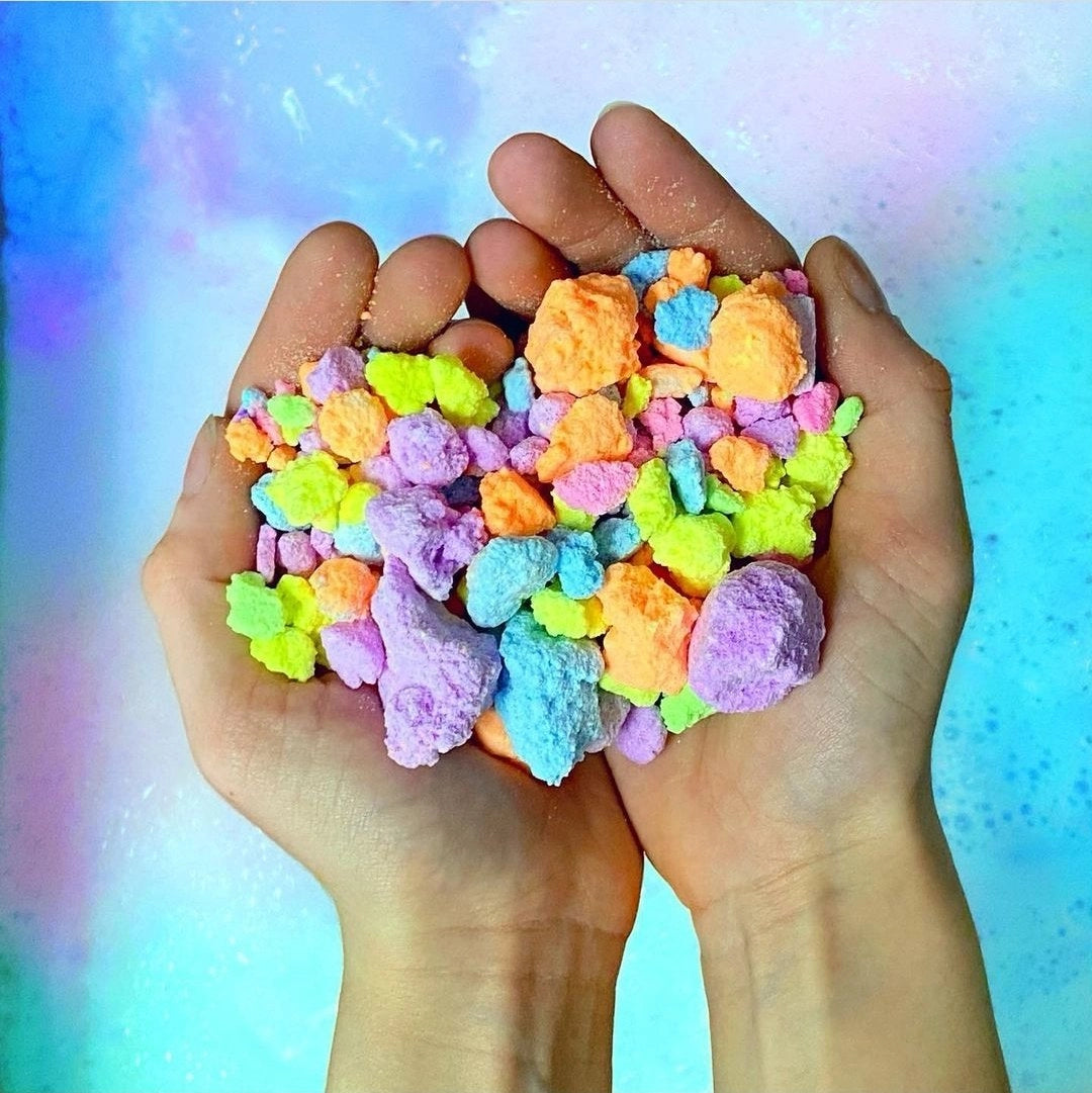 Hands holding colorful Pop Rocks Bath Fizzies with vibrant, pebble-sized chunks for a fun, fizzy bath experience.