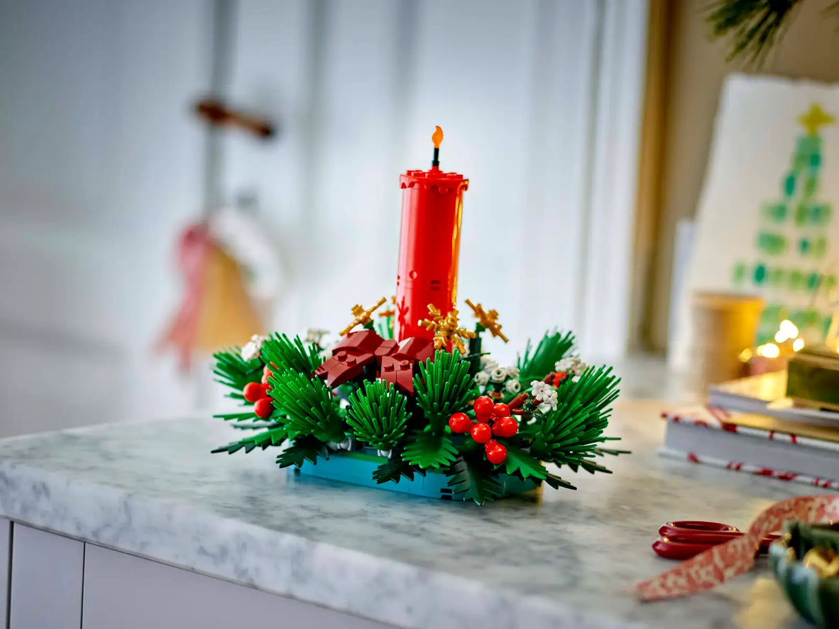 LEGO red candle surrounded by green foliage, red berries, and golden stars Christmas table decoration on marble surface