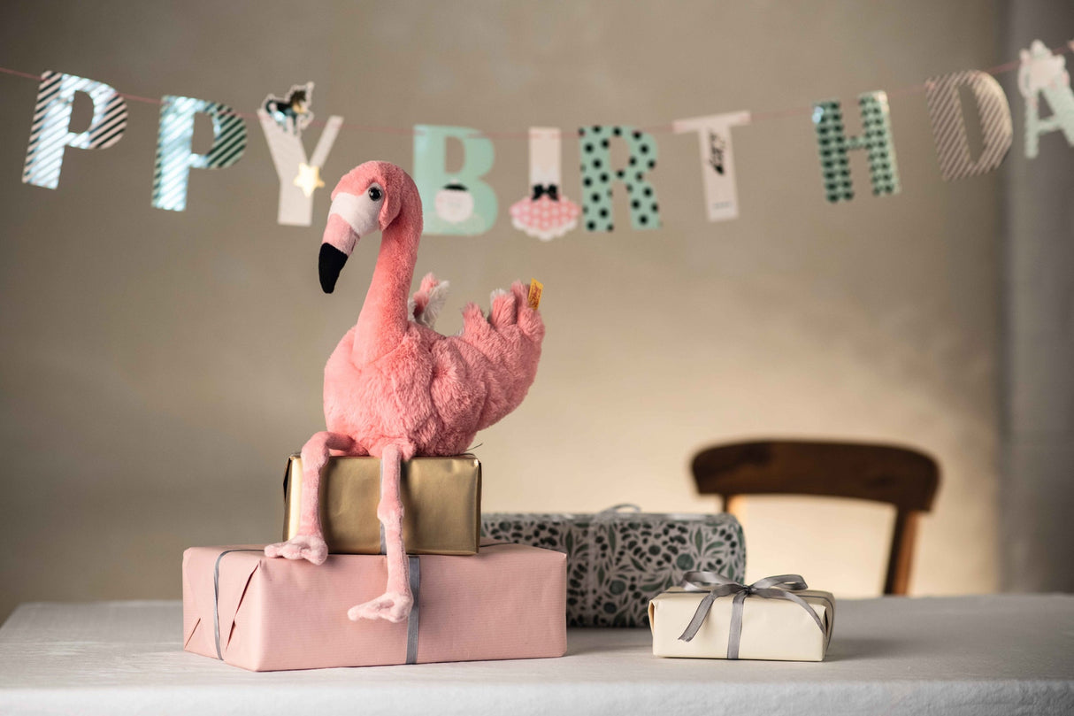 Flamingo Jill plush with dangling legs and bright pink plumage sitting on wrapped birthday gifts.
